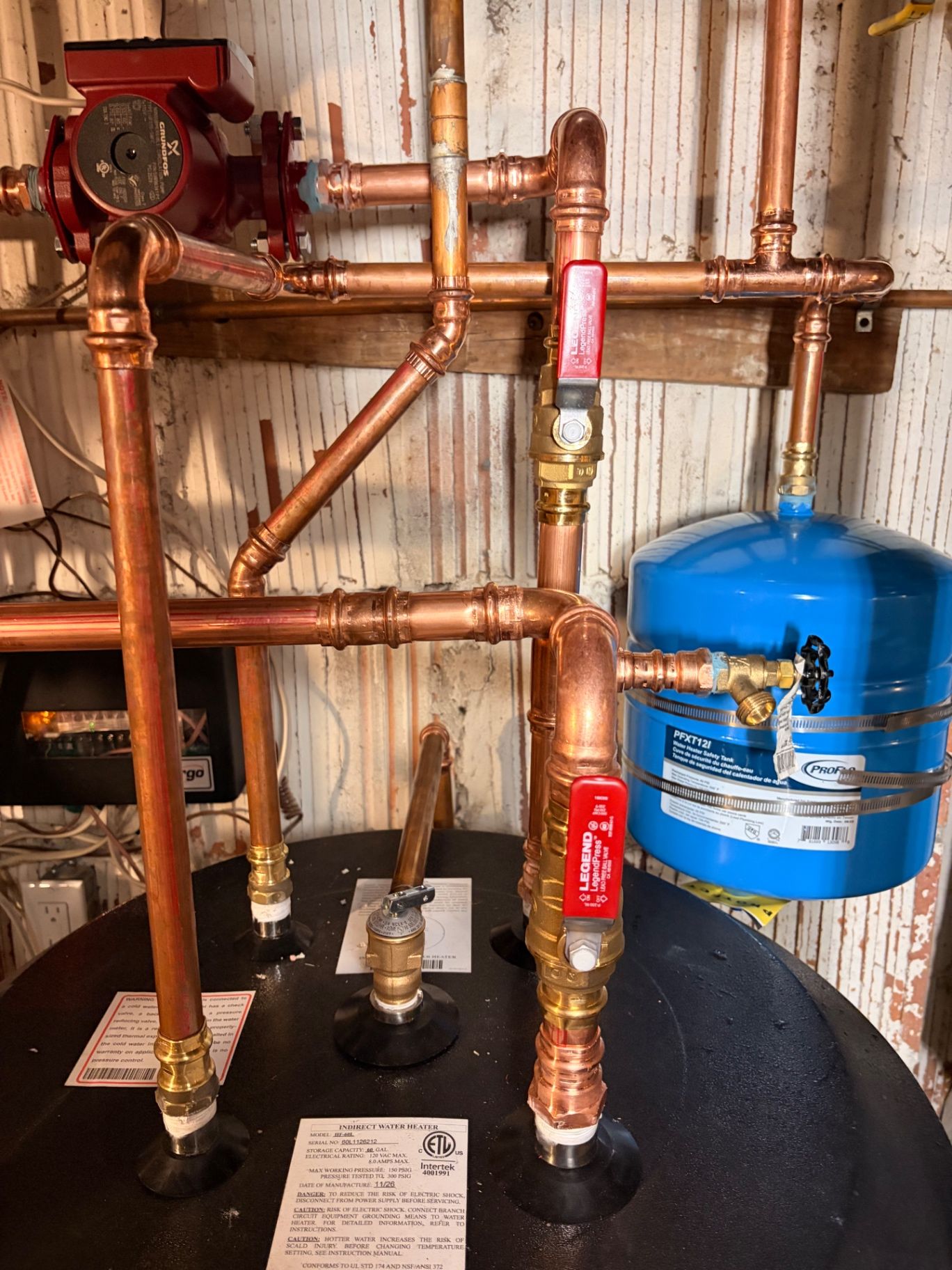 Copper plumbing, shutoff valves, and blue expansion tank assembly in a mechanical room